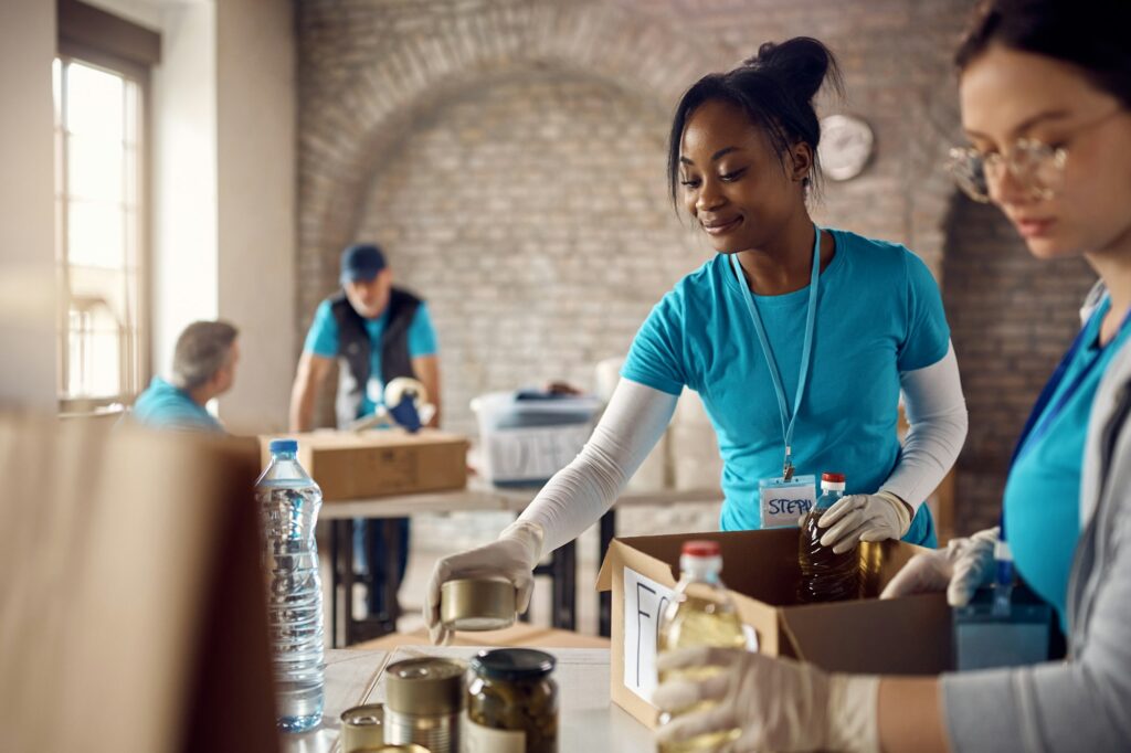 Happy African American volunteer packing food into donation boxes at charity center.